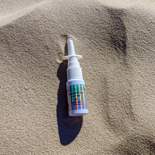 Nasal spray bottle with a colorful label on a sandy surface